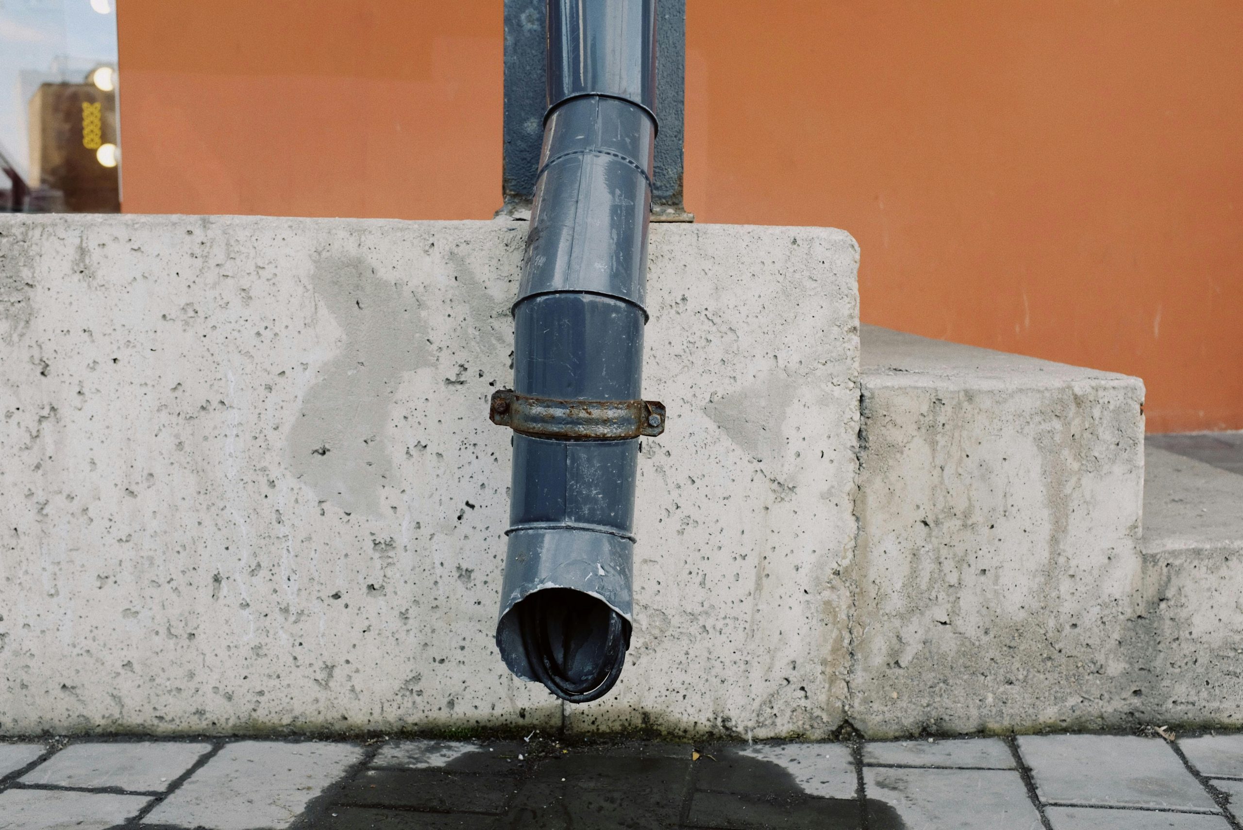 Aged metal drain pipe on a concrete wall with water stains, highlighting urban decay.